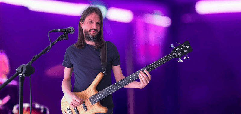 Fretless bass tutorial banner featuring a bearded man playing an electric fretless bass guitar beside a microphone, with purple stage lighting and the text “Fretless Bass Level 2: Make Your Bass Sing”.
